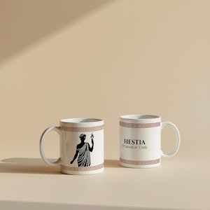 May include: Two white ceramic mugs with brown geometric border designs. One mug features a black illustration of a figure holding a torch. The other mug has the text "HESTIA Warmth & Unity" in black.