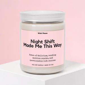 May include: A glass jar candle with a white lid and a pink label. The label reads "Night Shift Made Me This Way" with text about vending machine snacks. The candle is 255 grams.