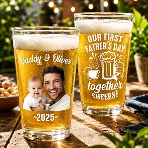 May include: Two pint glasses filled with beer. One glass has a photo of a man and baby with the text "Daddy & Oliver -2025-". The other glass has the text "OUR FIRST FATHER'S DAY together CHEERS!" in white.