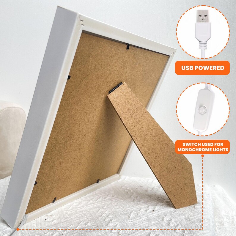 Pu&ograve; includere: Cornice bianca con retro marrone e cavalletto in legno. La cornice &egrave; alimentata tramite USB e ha un interruttore per luci monocromatiche. La cornice &egrave; su una superficie bianca.