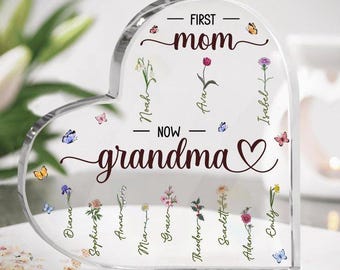 May include: A clear, heart-shaped acrylic plaque with the words "FIRST mom NOW grandma" in elegant script. The plaque features names, flowers, and butterflies, making it a personalized gift.