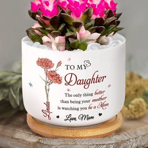 May include: White ceramic planter with a floral design and the text "TO MY Daughter". The planter contains a flowering succulent with pink blooms. The text reads "The only thing better than being your mother is watching you be a Mom."