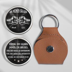 May include: A set of two round metal tokens and a brown leather keychain. The tokens have black backgrounds with white text and illustrations of clasped fists. The keychain has a silver ring and a brown leather fob.