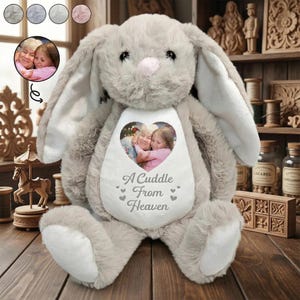 May include: A plush gray bunny rabbit with long ears and a pink nose. The bunny has a white heart-shaped patch on its chest with a photo of two people hugging. The text "A Cuddle From Heaven" is printed below the photo.