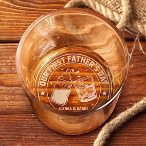 K&ouml;nnte beinhalten: Ein klares Whiskyglas mit ge&auml;tztem Text und Grafiken. Der Text lautet "OUR FIRST FATHER'S DAY" mit einer Babyflasche und einem Glas Whisky. Die Namen "GLORIA & DADDY" sind ebenfalls auf dem Glas ge&auml;tzt.