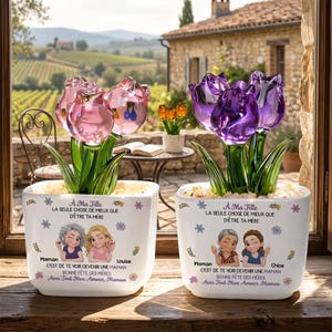 Peut inclure: Deux pots de fleurs décoratifs avec des sculptures de tulipes en verre. L'un présente des tulipes roses, l'autre violettes. Chaque pot a une base blanche avec un motif floral et du texte en français. Vue panoramique en arrière-plan.