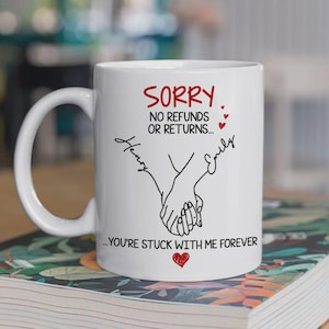 May include: White ceramic mug with a black line drawing of two hands holding each other. The mug has the text "SORRY, NO REFUNDS OR RETURNS... YOU'RE STUCK WITH ME FOREVER" in red and black. Names "Henry" and "Emily" are also on the mug.