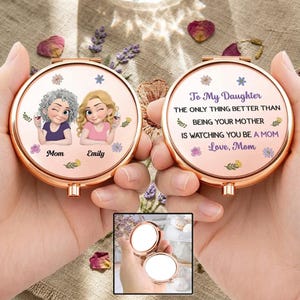 Könnte beinhalten: Ein roségoldener Kompaktspiegel mit personalisiertem Design. Eine Seite zeigt Illustrationen einer Mutter und Tochter mit den Namen "Mom" und "Emily". Die andere Seite hat den Text "To My Daughter...Love, Mom."