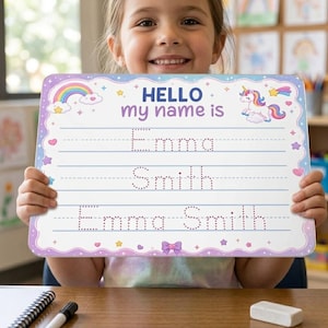 May include: A rectangular white dry-erase practice board with a scalloped purple border, featuring the text HELLO my name is, a rainbow, and a unicorn. The board includes three sets of dotted lines for tracing the names Emma and Smith.
