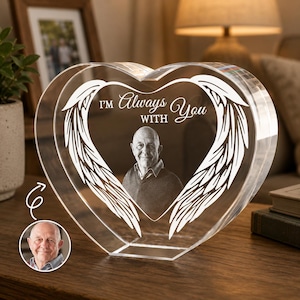 Könnte beinhalten: Ein klarer, herzförmiger Kristall-Fotorahmen mit einem Bild eines Mannes. Der Rahmen hat geätzte Engelsflügel und die Worte "I'm Always With You". Ein kleines Foto des Mannes befindet sich in der unteren linken Ecke.