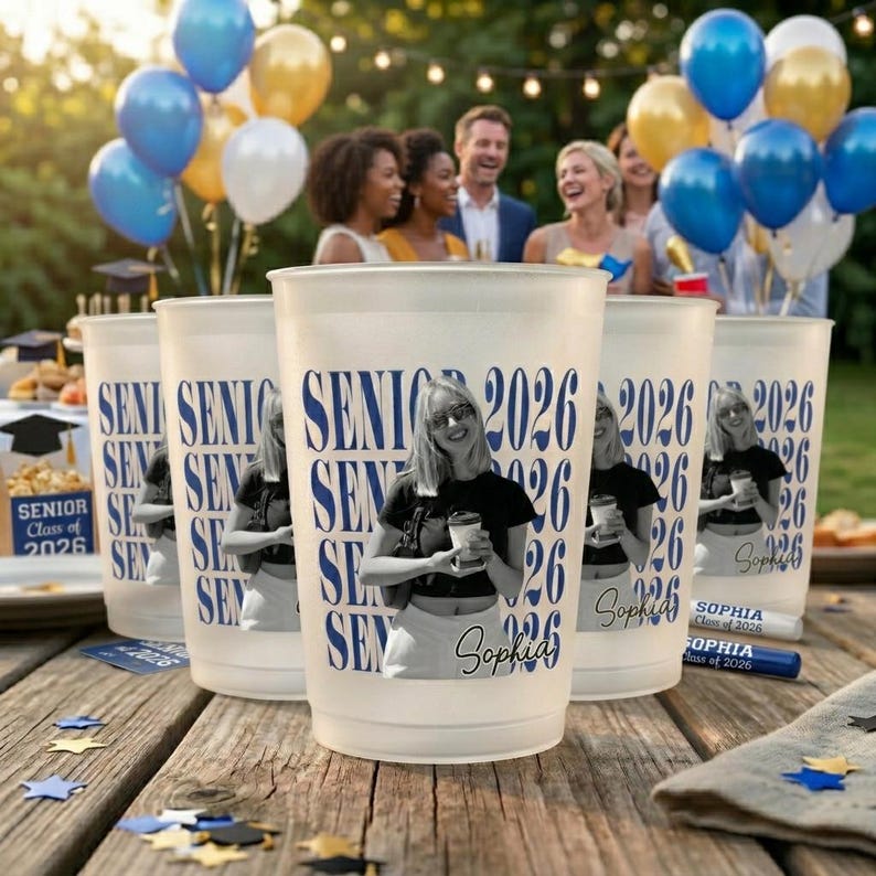 Pode incluir: Copos de pl&aacute;stico fosco com "SENIOR 2026" impresso em azul, com uma foto de uma pessoa. Os copos est&atilde;o em uma mesa de madeira, com bal&otilde;es ao fundo. Tema de festa de formatura.