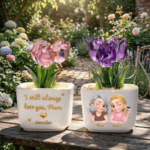 Peut inclure: Deux pots carrés blancs avec des fleurs de tulipes en verre. L'un a des tulipes roses et le texte "I will always love you, Mom" avec un cœur et le nom "Jennifer". L'autre a des tulipes violettes et des illustrations de deux femmes avec les noms "Mom" et "Jennifer".