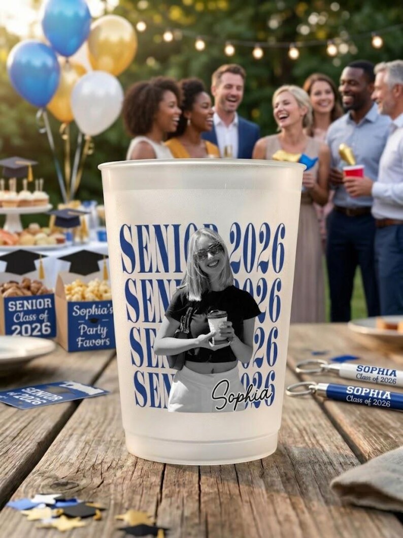 Pode incluir: Um copo de pl&aacute;stico fosco com o texto "SENIOR 2026" em azul. Uma foto em preto e branco de uma pessoa est&aacute; na x&iacute;cara. O nome "Sophia" tamb&eacute;m est&aacute; na x&iacute;cara. Lembrancinhas de festa e bal&otilde;es est&atilde;o ao fundo.