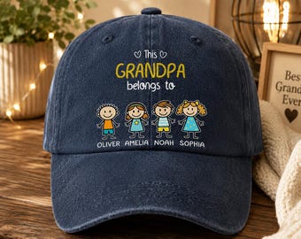 May include: A navy blue baseball cap with the text "This Grandpa belongs to" in yellow and white. Below the text are four cartoon children's figures with the names Oliver, Amelia, Noah, and Sophia. The cap is on a wooden surface.