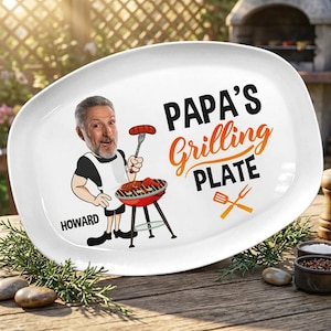Può includere: Piatto ovale bianco con la scritta "PAPA'S Grilling PLATE" e un'illustrazione a cartoni animati di un uomo che griglia. L'uomo indossa un grembiule bianco e nero e il nome "HOWARD" è stampato.
