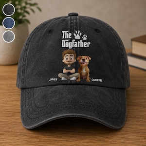 May include: A black baseball cap with the text "The Dogfather" and paw prints. The cap features a cartoon illustration of a man and a dog, with the names "James" and "Cooper" below. The cap is made of a soft, worn material.