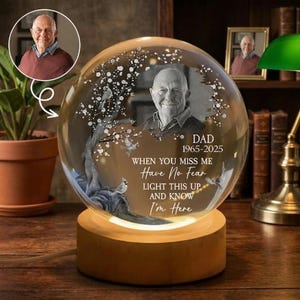 May include: A personalized memorial night light with a photo of a man inside a glass sphere. The sphere sits on a wooden base that emits a warm glow. Text reads "DAD 1965-2025 WHEN YOU MISS ME Have No Fear LIGHT THIS UP AND KNOW I'm Here."