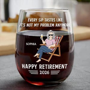 Puede incluir: Una copa de vino sin pie llena de l&iacute;quido rojo. La copa presenta una ilustraci&oacute;n de dibujos animados de una mujer con gafas de sol relaj&aacute;ndose en una silla de playa, sosteniendo una copa de vino. El texto en la copa dice "EVERY SIP TASTES LIKE IT'S NOT MY PROBLEM ANYMORE" y "HAPPY RETIREMENT 2026."