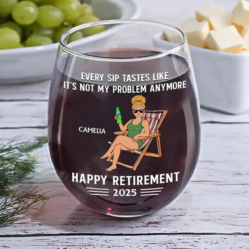 Puede incluir: Una copa de vino sin pie llena de l&iacute;quido rojo. La copa presenta un gr&aacute;fico de una mujer en una silla de playa con el texto "EVERY SIP TASTES LIKE IT'S NOT MY PROBLEM ANYMORE" y "HAPPY RETIREMENT 2025". El nombre "CAMELIA" tambi&eacute;n est&aacute; impreso en la copa.