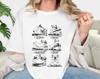 May include: White t-shirt featuring a black and white illustration of a French Bulldog performing Pilates exercises. The design includes four different poses with the text: "1. LEG STRETCH", "2. STRAP PULL", "3. BALANCE STFETCH", and "4. PUSH BAR".