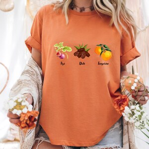 May include: Orange t-shirt with a graphic of figs, dates, and tangerines. The text below each fruit reads "Figs", "Date", and "Tangerine".
