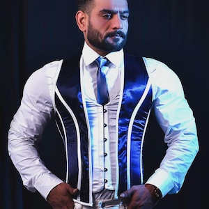 May include: A man wearing a white shirt, a blue and white striped vest, and a dark blue tie. He is standing with his hands in his pockets.