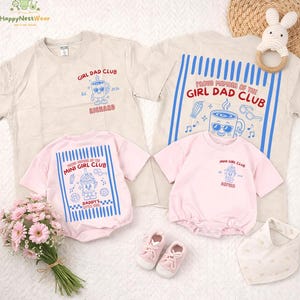 May include: A collection of baby and toddler apparel, including two beige t-shirts and two pink rompers. The shirts and rompers feature the text "GIRL DAD CLUB" and "MINI GIRL CLUB" with cartoon graphics. Accessories include baby shoes, a bib, and a bunny-shaped teether.