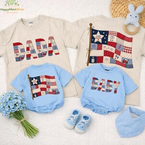 Puede incluir: Una colección de ropa infantil, que incluye camisetas beige claro con "DADA" y un diseño de bandera, y peleles azul claro con "BABY" y un diseño de bandera. También hay zapatos azules, un babero, un juguete de madera y flores.