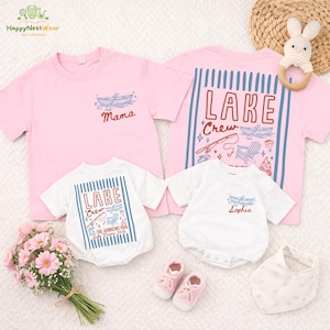May include: Pink and white matching family shirts and onesies with lake-themed designs. The pink shirts have "Mama" and a boat graphic. The white onesies and pink shirt feature "Lake Crew" and lake-related illustrations. Includes baby shoes and a bib.