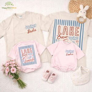 May include: A collection of matching family apparel, including beige and pink t-shirts and onesies. The shirts feature boat and lake-themed graphics with text that reads "Dada", "LAKE Crew", and "Sophia". Accessories include baby shoes and a bib.
