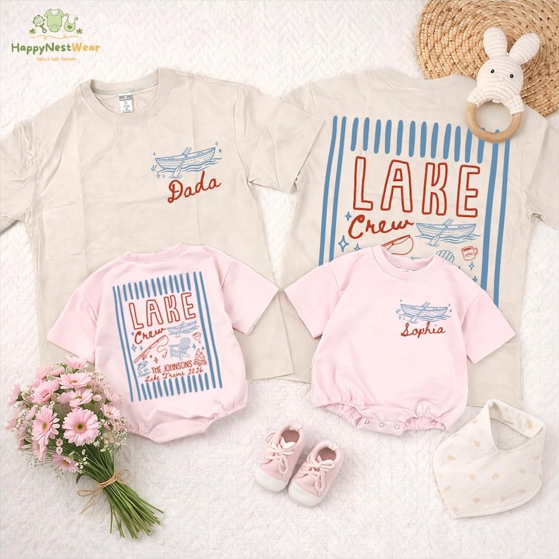 May include: A collection of matching family apparel, including beige and pink t-shirts and onesies. The shirts feature boat and lake-themed graphics with text that reads "Dada", "LAKE Crew", and "Sophia". Accessories include baby shoes and a bib.