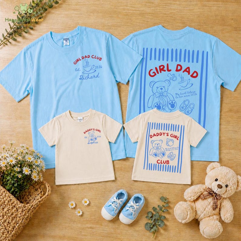 May include: Four light blue and cream-colored t-shirts with text and graphics. The shirts say "GIRL DAD CLUB" and "DADDY'S GIRL CLUB". There are also baby shoes and a teddy bear. The shirts are for a family.