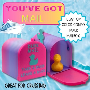 May include: A custom color mailbox featuring a pink front panel with the text DUCK MAIL, TAKE A DUCK, LEAVE A DUCK, and a teal duck silhouette. The mailbox body has a purple and blue gradient, and a yellow rubber duck sits inside the open compartment.