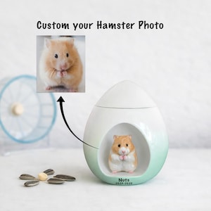 May include: A white and mint green ceramic hamster-themed container with a hamster figurine inside. The text "Custom your Hamster Photo" is at the top. A photo of a hamster is above the container. Sunflower seeds are at the bottom.