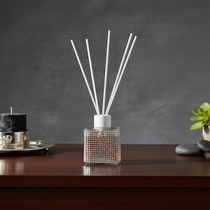 Könnte beinhalten: Eine transparente Glas-Diffusorflasche mit weißem Deckel und weißen Stäbchen. Die Flasche hat ein strukturiertes, gepunktetes Muster. Eine schwarze Kerze in einem silbernen Halter und eine kleine Sukkulente sind ebenfalls zu sehen.