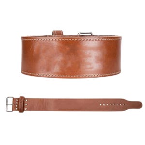 Peut inclure: Une ceinture d'halt&eacute;rophilie en cuir marron avec des coutures blanches et une boucle argent&eacute;e. La ceinture est large et con&ccedil;ue pour soutenir pendant les exercices de levage lourds. La ceinture est montr&eacute;e avec sa sangle.