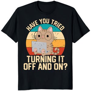 May include: Black t-shirt featuring a cartoon cat wearing glasses and using a laptop. The cat is set against a retro sunset design with the text "HAVE YOU TRIED TURNING IT OFF AND ON?" in white.