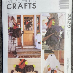 May include: A McCall's Crafts sewing pattern for Halloween decorations. The pattern includes instructions for making a witch, a ghost, and a black cat. The pattern is for a door decoration, and the image shows the finished decorations on a door.