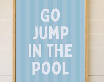 Könnte beinhalten: Ein gerahmter Wandkunstdruck mit den weißen Worten "GO JUMP IN THE POOL" auf hellblau gestreiftem Hintergrund. Der Druck hängt über einem cremefarbenen Sofa mit einem marineblauen Kissen und einem Korbstuhl mit passendem Kissen.