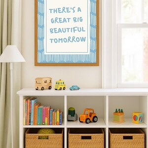 May include: A framed print with the text "THERE'S A GREAT BIG BEAUTIFUL TOMORROW" hangs above a white shelf. The shelf displays wooden toy vehicles, books, and woven storage baskets. The color scheme is light and airy.