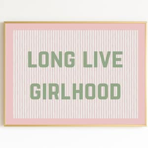 Puede incluir: Un estampado enmarcado con las palabras "LONG LIVE GIRLHOOD" en letras verdes. El fondo es rosa claro con líneas blancas verticales. El marco es dorado con un borde rosa.