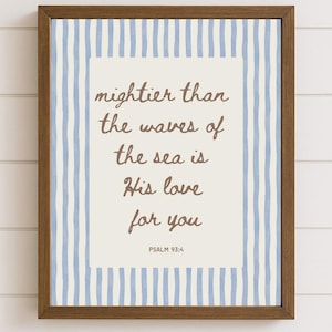May include: Framed wall art with a brown wooden frame. The artwork features a cream-colored background with blue vertical stripes and a central panel with the text "mightier than the waves of the sea is His love for you" and "PSALM 93:4" in brown script.