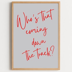 May include: A framed print with a light gray background and red handwritten text that reads, "Who's That coming down The Track?" The frame is made of light-colored wood.