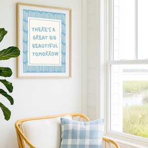 May include: A framed print with the text "THERE'S A GREAT BIG BEAUTIFUL TOMORROW" in blue. The print hangs above a wicker chair with a blue and white plaid pillow. A window and greenery are visible in the background.