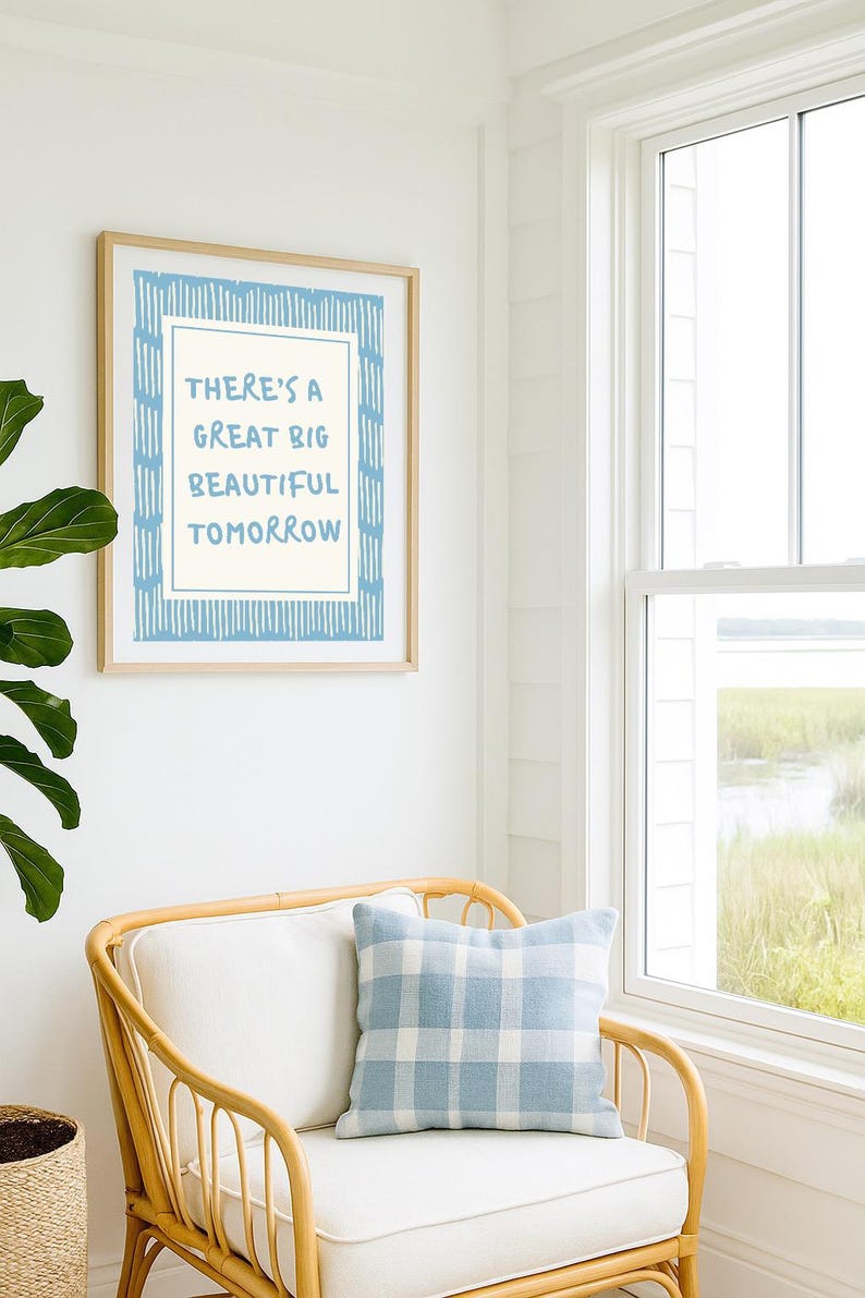 May include: A framed print with the text "THERE'S A GREAT BIG BEAUTIFUL TOMORROW" in blue. The print hangs above a wicker chair with a blue and white plaid pillow. A window and greenery are visible in the background.