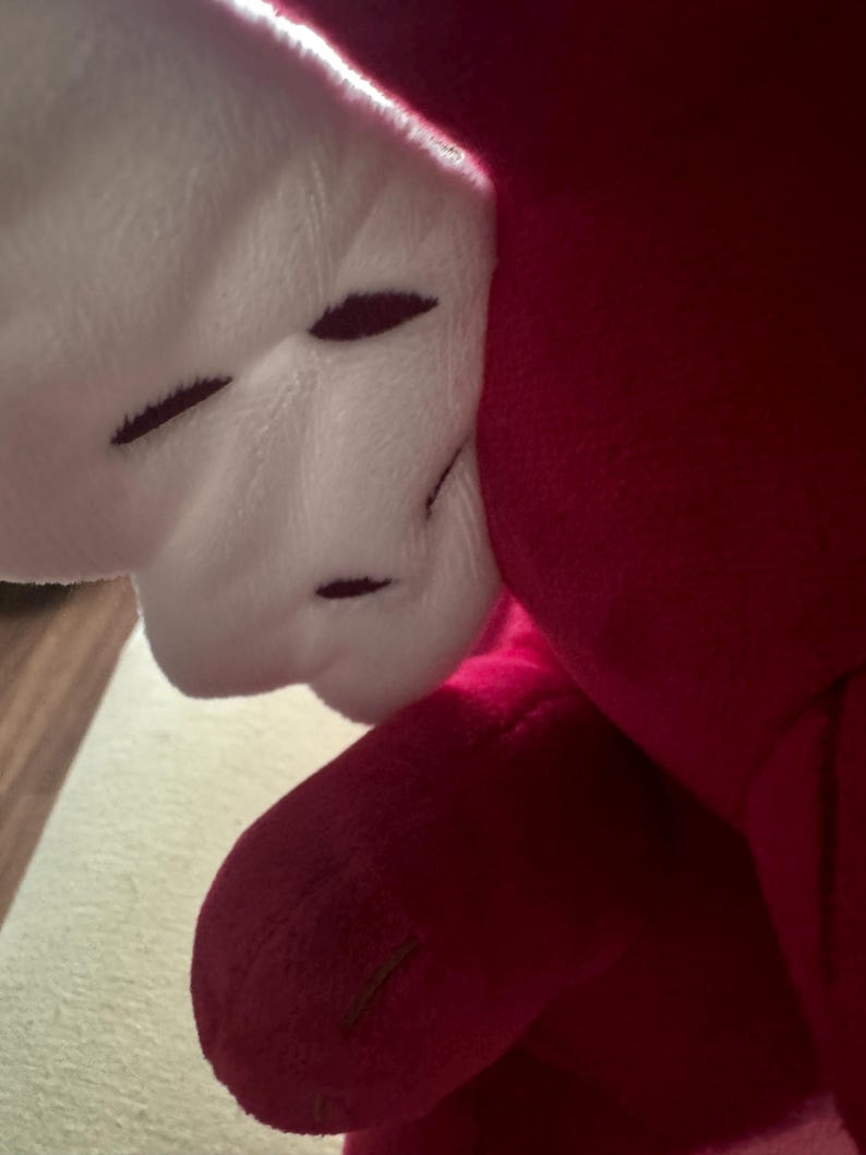 May include: Close-up of a plush toy featuring a white, textured wing with dark brown stitched details. The wing is attached to a vibrant red body, with a soft, velvety texture. The toy's design suggests a whimsical or fantasy theme.
