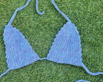 May include: A handmade, blue crochet bikini top with triangle cups and tie straps. The top is made of a soft, textured yarn and is displayed on a green grassy surface. The top has a scalloped edge.