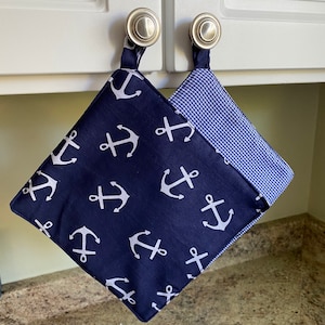 May include: A pair of blue and white pot holders with an anchor pattern hanging on cabinet knobs. One pot holder is blue with white anchors and the other is white with blue gingham.