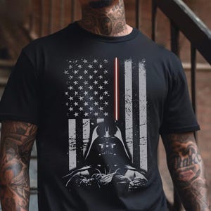 May include: Black t-shirt featuring a graphic of Darth Vader's helmet and a lightsaber, integrated into a distressed American flag design. The shirt has a crew neck and short sleeves, suitable for casual wear.