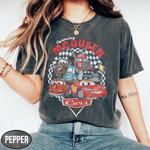 Puede incluir: Camiseta gris oscuro con un gr&aacute;fico de personajes de la pel&iacute;cula Cars, incluyendo a Rayo McQueen. El dise&ntilde;o incluye el texto "Lightning McQueen" y "Cars" en un tema de carreras. La camiseta tiene un aspecto vintage y desgastado.
